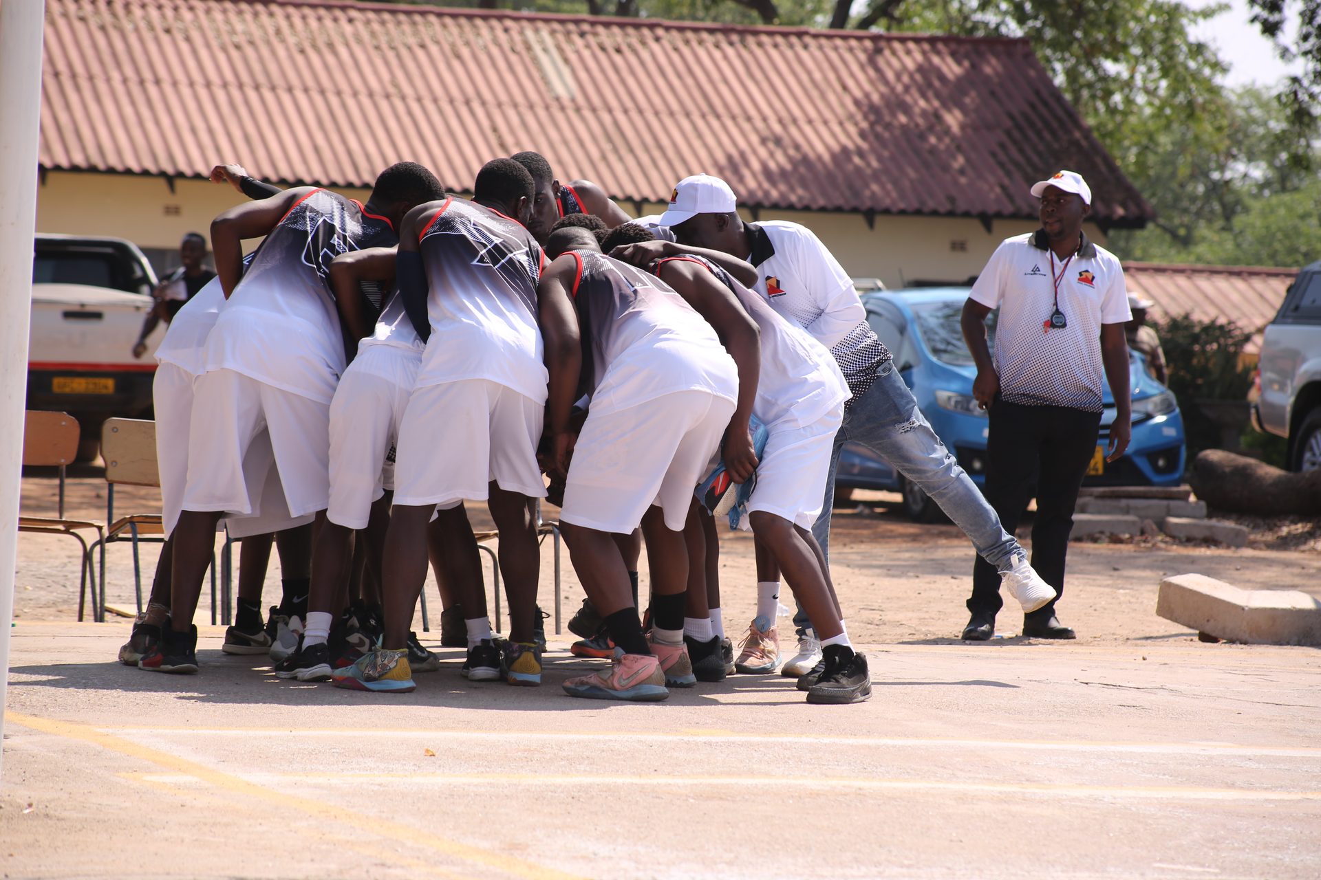 Players huddle before a match as a coach walks the sideline in Matabeleland North